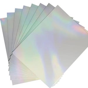 May include: A stack of rectangular sheets of paper with a smooth, reflective surface that displays a holographic, iridescent effect. The sheets are layered in a fan-like arrangement, showing a spectrum of light colors against a silver base.