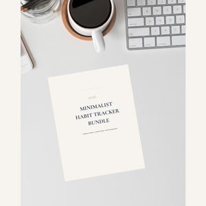 May include: A minimalist habit tracker bundle with the year 2026 printed on the top. The text is in a navy blue font. A white coffee cup with dark coffee sits on a wooden coaster. A computer keyboard and a glass jar with pencils are also visible.