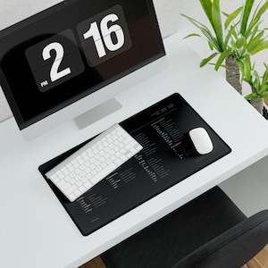 May include: A rectangular black desk mat featuring a white printed reference guide for computer keyboard shortcuts. The mat is positioned on a white desk surface with a white wireless keyboard and a white computer mouse placed on top of the mat.