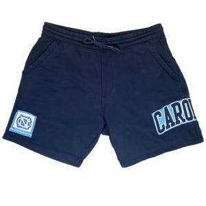 Puede incluir: Pantalones cortos azul marino con cintura con cordón y bolsillos laterales. Los pantalones cortos tienen un parche con un logotipo en la pierna izquierda y la palabra "CARO" en azul claro y blanco en la pierna derecha.