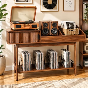 May include: A walnut-toned wooden record player console featuring a slatted cabinet door, a top surface holding a tan portable turntable and two black speakers, and a lower shelf with four metal dividers organizing vinyl record collections.