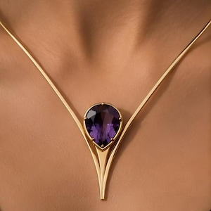 May include: A gold necklace featuring a central pear-shaped purple gemstone set in a prong setting. The metal frame extends upward from the stone into two smooth, tapered arms that form a V-shape, connecting to a thin gold chain on each side.