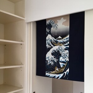 May include: A white closet with shelves and a sliding door. The door is open and reveals a room with a blue and white tapestry hanging on the wall. The tapestry depicts a large wave with a boat and people in it.