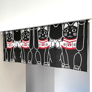 Puede incluir: Cortina japonesa Maneki Neko en blanco y negro. La cortina presenta un patr&oacute;n repetido de gatos negros estilizados con patas levantadas, collares rojos y detalles blancos. La cortina cuelga en una puerta.