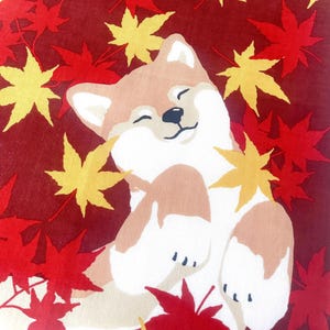 May include: A fabric textile featuring a tan and white Shiba Inu dog with a happy expression, surrounded by scattered red and yellow maple leaves against a deep maroon background. The dog is depicted lying down with its eyes closed and paws raised.
