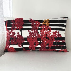 May include: Rectangular decorative pillow with a striking design. The pillow features a pattern of red and gold tree branches against a backdrop of black and white horizontal stripes. The pillow is a decorative home accent.