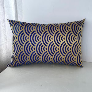 Può includere: Un cuscino decorativo blu e oro con un motivo geometrico. Il cuscino è realizzato in un tessuto morbido e soffice e ha un leggero bagliore.