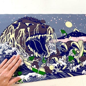 May include: A blue and white print of a monster emerging from the ocean waves. The monster has a large mouth with sharp teeth and is dripping with a yellow substance. The print also features a mountain in the background and a cherry blossom tree.