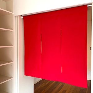 May include: A red fabric room divider with three panels hangs from a track system. The divider is in front of a white closet with shelves.