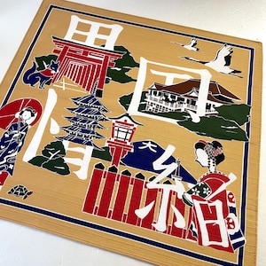 以下が含まれることがあります： ベージュの布製のランチョンマットに、カラフルな日本のデザインが施されています。デザインには、赤い鳥居、五重塔、山、傘を持った女性、着物を着た女性、日本語の文字が描かれています。