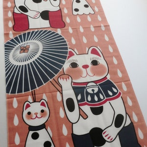May include: A pink fabric panel with a repeating pattern of white cats holding umbrellas. The cats are wearing red and blue clothing and have black spots. The background is a light pink with white raindrops.