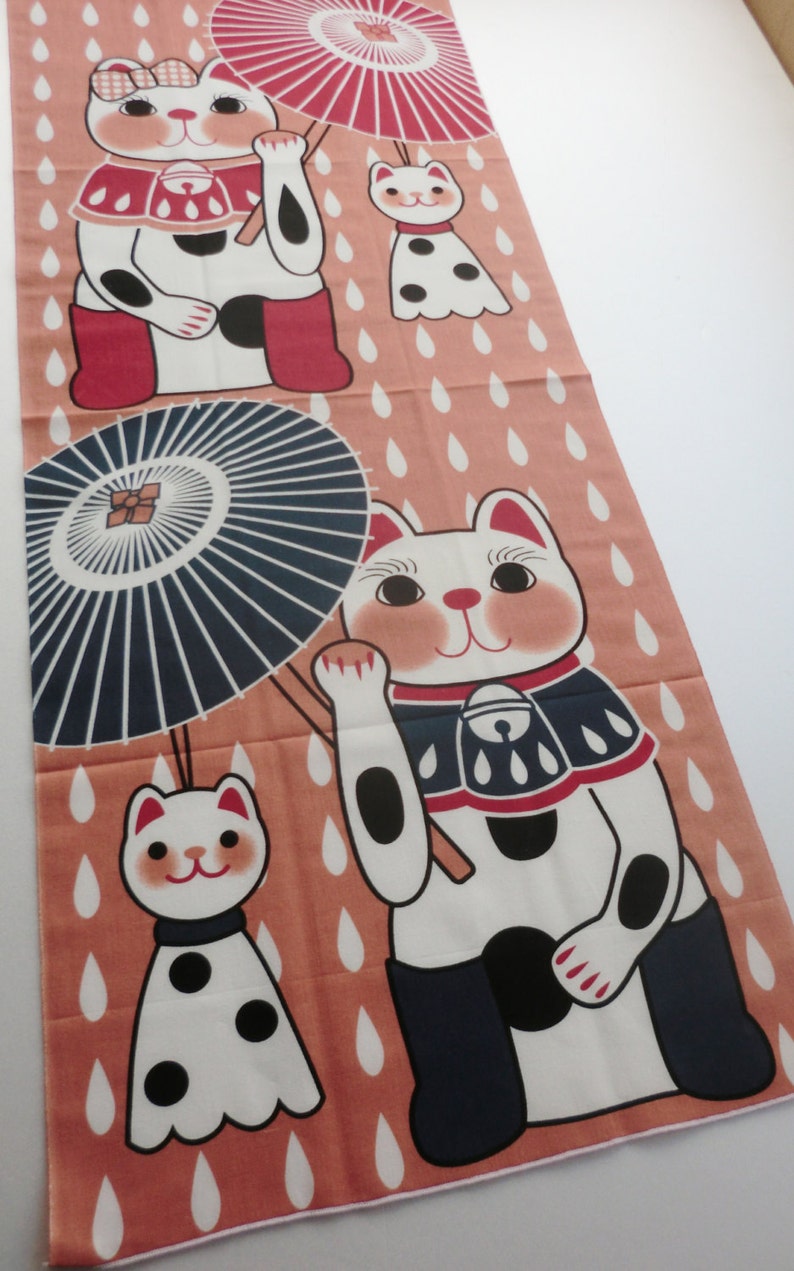 May include: A pink fabric panel with a repeating pattern of white cats holding umbrellas. The cats are wearing red and blue clothing and have black spots. The background is a light pink with white raindrops.