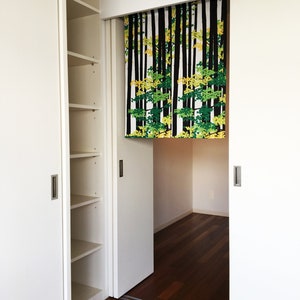 May include: White sliding closet doors with a black and green patterned fabric hanging in the middle. The fabric has a design of trees with black trunks and green and yellow leaves.