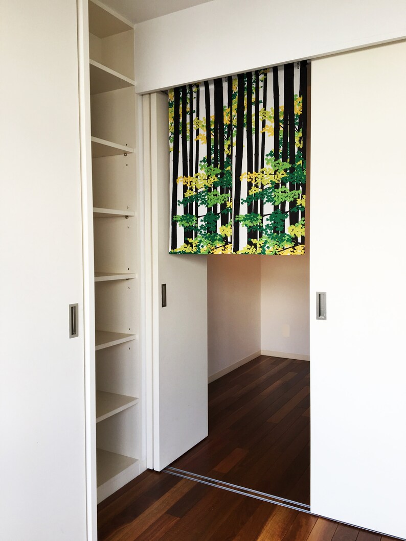 May include: White sliding closet doors with a black and green patterned fabric hanging in the middle. The fabric has a design of trees with black trunks and green and yellow leaves.