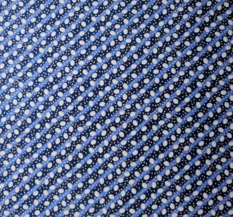 May include: Close-up of a fabric with a repeating pattern of white oval shapes and small pink and brown accents on a navy blue background. The pattern is arranged in diagonal rows, separated by light blue stripes.