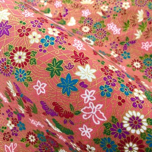 May include: Pink fabric with a floral pattern featuring a variety of flowers in red, white, blue, green, and purple. The fabric has a subtle gold shimmer.