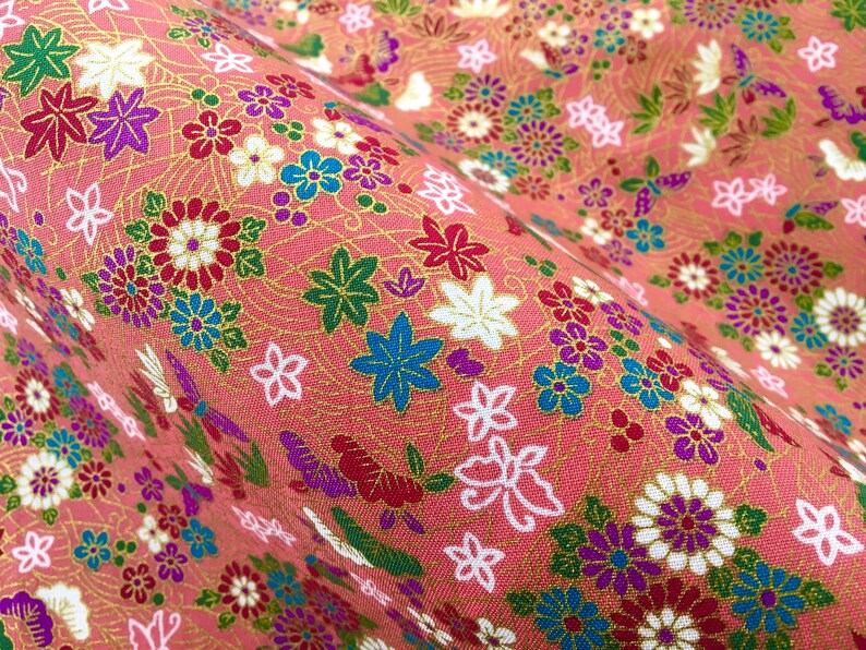 May include: Pink fabric with a floral pattern featuring a variety of flowers in red, white, blue, green, and purple. The fabric has a subtle gold shimmer.