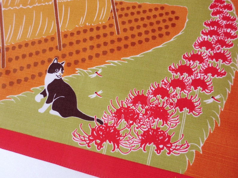 May include: A black and white cat with green eyes sits on a green background with red spider lily flowers and dragonflies. The background is a field of orange and brown.