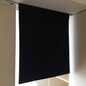 May include: A black blackout curtain is hanging from a track system. The curtain is fully extended and is covering a window. The curtain is made of a thick, opaque fabric.