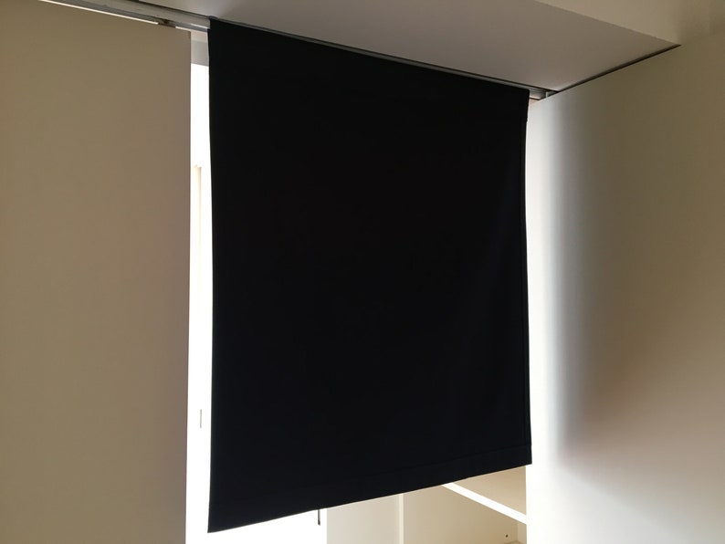 May include: A black blackout curtain is hanging from a track system. The curtain is fully extended and is covering a window. The curtain is made of a thick, opaque fabric.