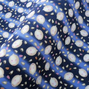 May include: Close-up of a fabric with a repeating pattern of white bunny-like figures with pink accents, set against a navy blue and light blue striped background. Small orange and pink petal-like shapes are scattered throughout the design.