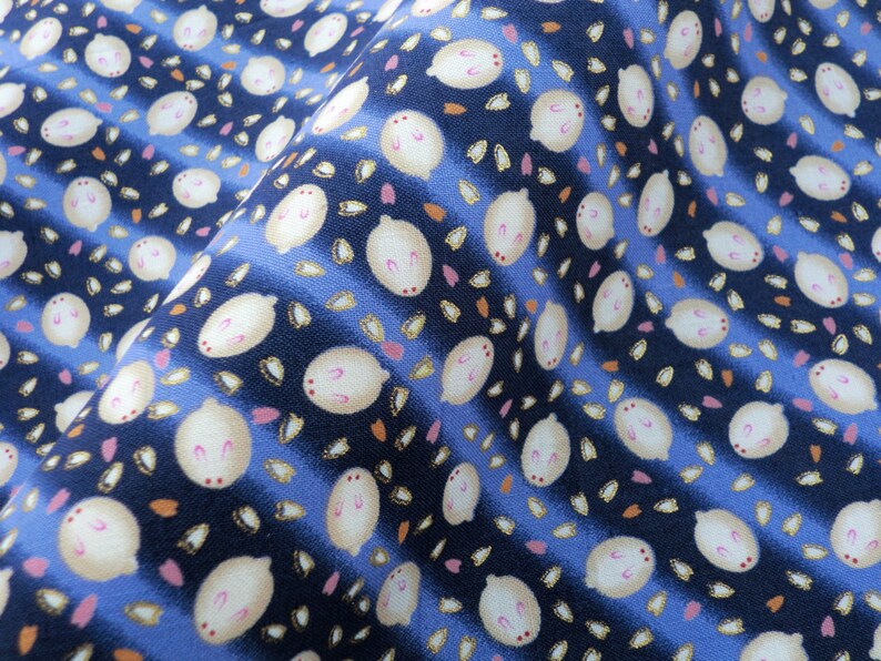 May include: Close-up of a fabric with a repeating pattern of white bunny-like figures with pink accents, set against a navy blue and light blue striped background. Small orange and pink petal-like shapes are scattered throughout the design.