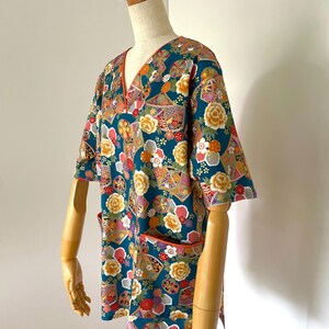 Puede incluir: Camiseta de manga corta azul turquesa con un estampado floral y geom&eacute;trico colorido. La camisa tiene cuello en V y un bolsillo en el lado izquierdo.