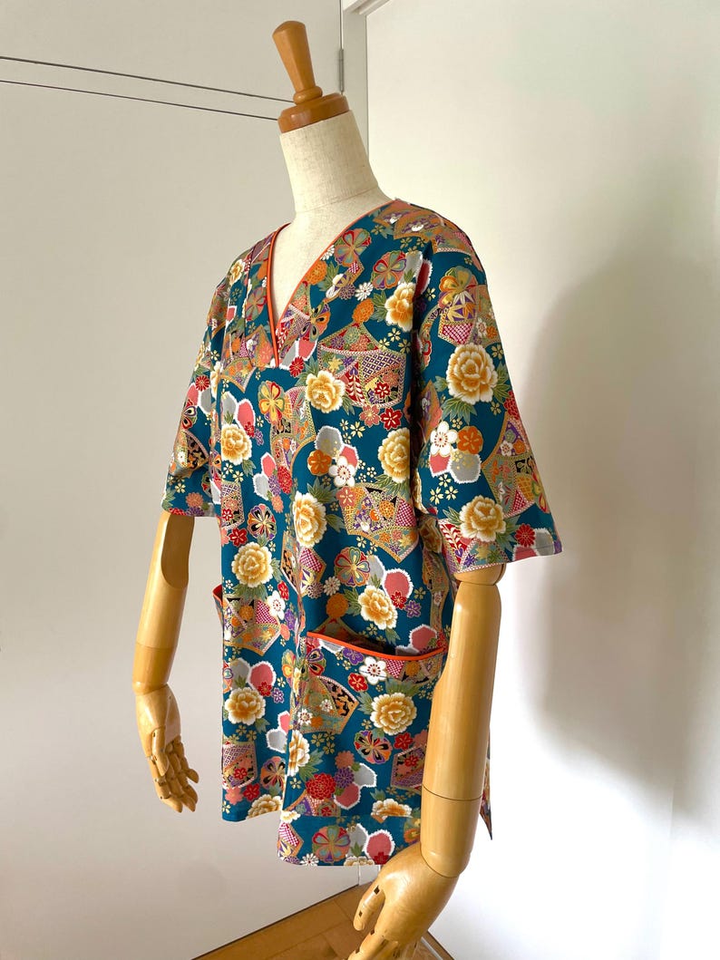 Puede incluir: Camiseta de manga corta azul turquesa con un estampado floral y geom&eacute;trico colorido. La camisa tiene cuello en V y un bolsillo en el lado izquierdo.