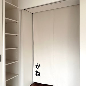 Puede incluir: Puertas de armario blancas con un sistema de rieles deslizantes. Las puertas est&aacute;n cerradas y tienen un car&aacute;cter japon&eacute;s negro "か" en la parte delantera.