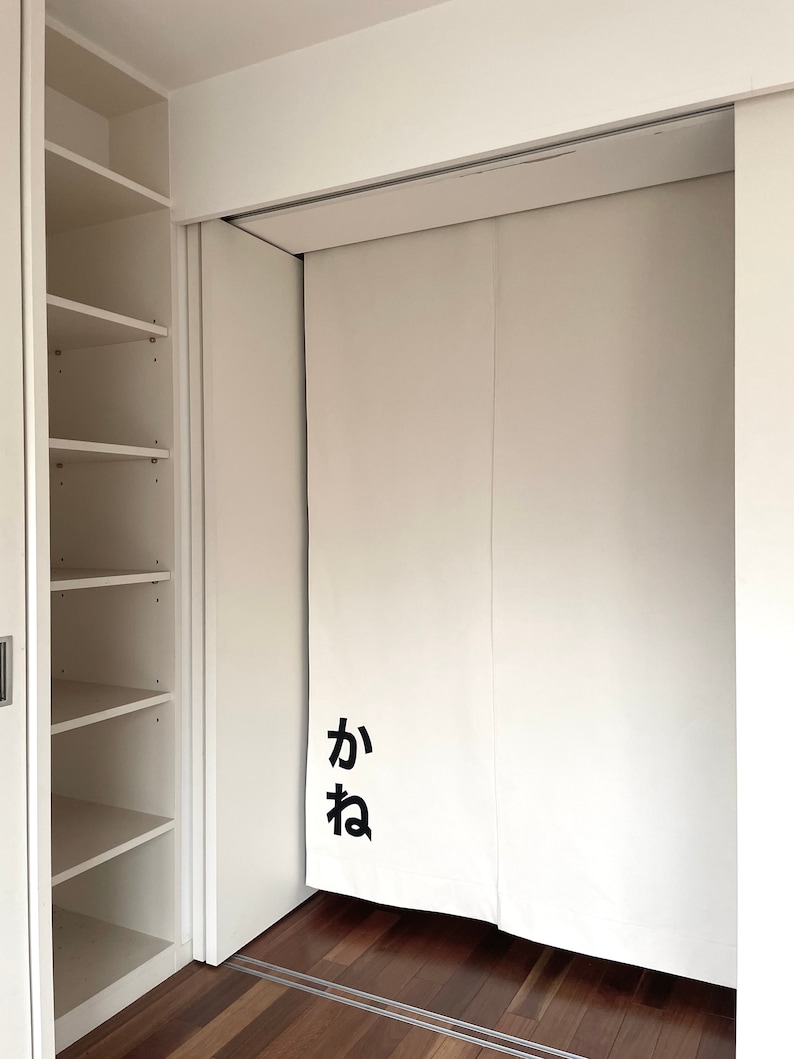 Puede incluir: Puertas de armario blancas con un sistema de rieles deslizantes. Las puertas est&aacute;n cerradas y tienen un car&aacute;cter japon&eacute;s negro "か" en la parte delantera.