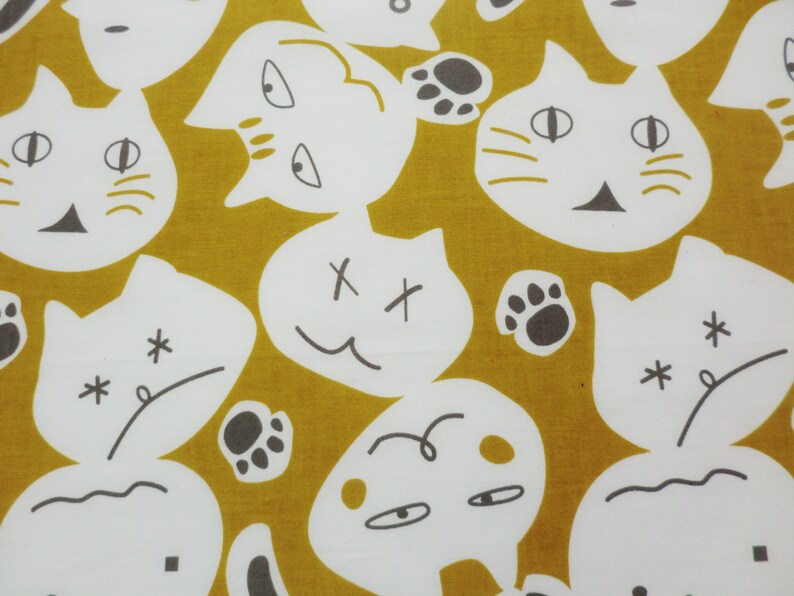 May include: A mustard yellow fabric with a white repeating pattern of cat faces and other abstract designs. The cat faces have different expressions, including happy, sad, and surprised. Some of the designs include paw prints and stars.