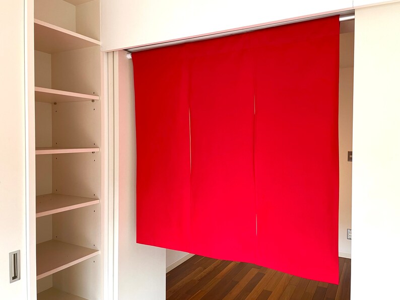 May include: A red fabric room divider with three panels hangs from a track system. The divider is in front of a white closet with shelves.