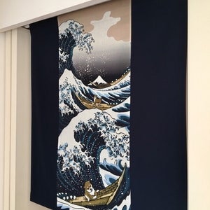 May include: A blue and white tapestry featuring a large wave with a small boat and two dogs. The tapestry is hanging on a white wall.