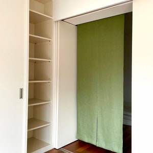 Puede incluir: Un armario blanco con puertas correderas y estantes. El armario est&aacute; abierto y los estantes est&aacute;n vac&iacute;os. Hay un divisor de habitaci&oacute;n de tela verde detr&aacute;s del armario.