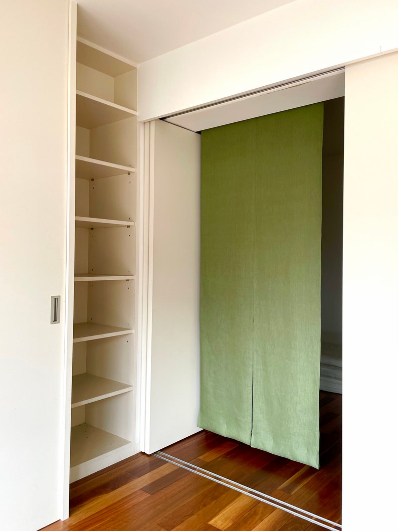 Puede incluir: Un armario blanco con puertas correderas y estantes. El armario est&aacute; abierto y los estantes est&aacute;n vac&iacute;os. Hay un divisor de habitaci&oacute;n de tela verde detr&aacute;s del armario.