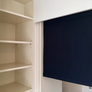 May include: A white closet with three shelves and a dark blue roller shade.