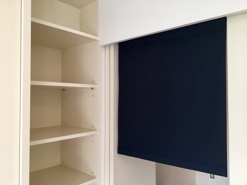May include: A white closet with three shelves and a dark blue roller shade.