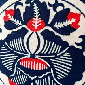 Op de afbeelding: Een blauw en wit kussen met een rood bloemenontwerp. Het kussen heeft een gestileerde bloem met een centrale stengel en bladeren.