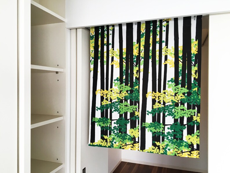 May include: A white, black, green, and yellow patterned curtain with a forest scene. The curtain is hanging in a doorway.