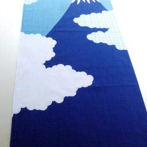 May include: A rectangular textile featuring a graphic print of a mountain with a white snow-capped peak against a large red sun. The background transitions from light blue at the top to dark blue at the bottom, accented by white clouds.