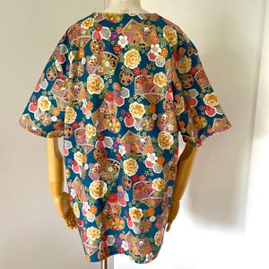 Puede incluir: Una camisa de manga corta azul turquesa con un estampado floral y geom&eacute;trico colorido. El estampado presenta colores dorados, rosas, rojos, blancos y morados.