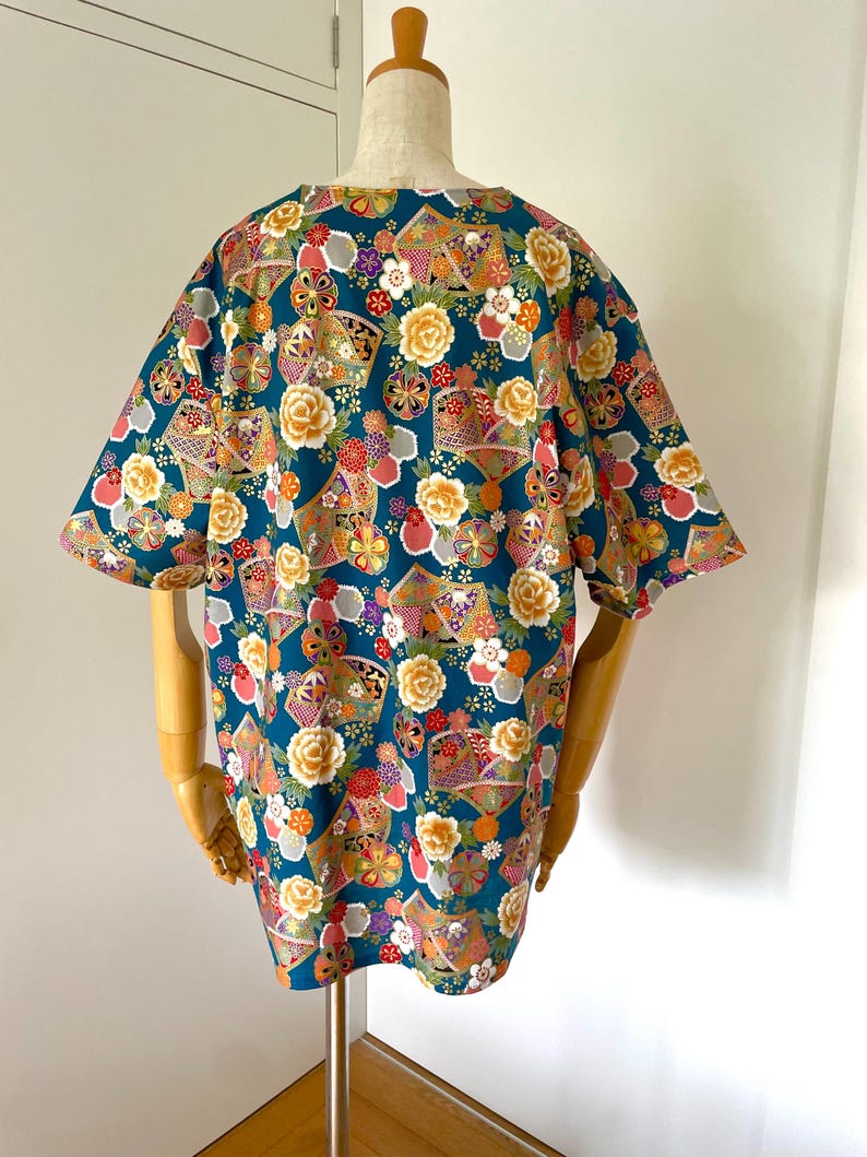 Puede incluir: Una camisa de manga corta azul turquesa con un estampado floral y geom&eacute;trico colorido. El estampado presenta colores dorados, rosas, rojos, blancos y morados.