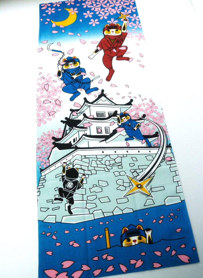 May include: A rectangular fabric panel featuring a colorful illustration of cats dressed as ninjas in action around a white castle. The scene includes falling pink cherry blossoms, a yellow crescent moon, and blue gradient sky and water elements.