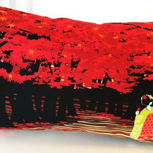 May include: A red and black pillow with a Japanese-inspired design. The pillow features a silhouette of a woman in a traditional kimono standing in front of a forest of red trees. The trees are silhouetted against a black background.