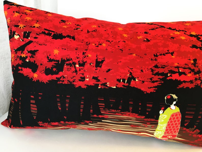 May include: A red and black pillow with a Japanese-inspired design. The pillow features a silhouette of a woman in a traditional kimono standing in front of a forest of red trees. The trees are silhouetted against a black background.