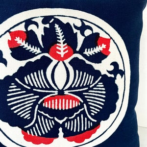 Op de afbeelding: Een marineblauw kussen met een wit cirkelvormig ontwerp met een gestileerd rood en zwart bloemenpatroon.