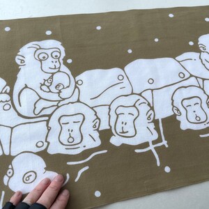 May include: A brown and white fabric with a repeating pattern of cartoon monkeys. The monkeys are white with brown outlines and are depicted in various poses, some holding babies. The background is a solid brown color with white dots.