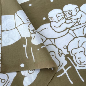 May include: Olive green and white fabric featuring a repeating pattern of cartoon monkeys. The monkeys are depicted in a playful, stylized manner, with white outlines against the olive background. The fabric is folded, showing both sides.