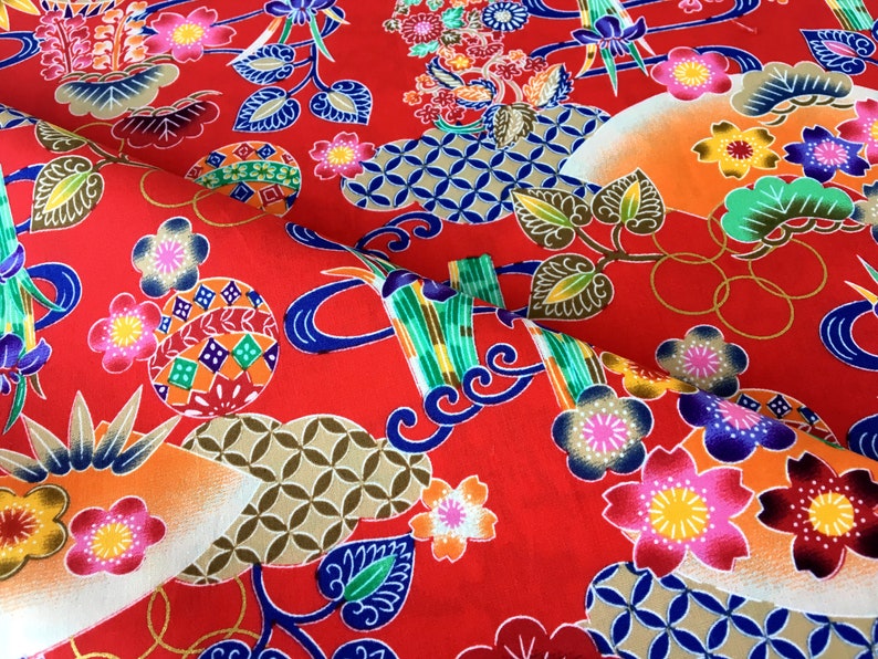May include: Red fabric with a repeating pattern of colorful flowers, geometric shapes, and stylized bamboo. The fabric has a traditional Japanese design.