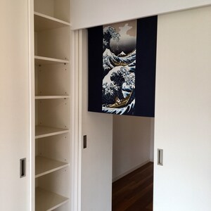 May include: White closet with sliding doors and shelves. The sliding doors are open to reveal a room with a wooden floor. A Japanese-style room divider with a blue and white wave design hangs on the door.